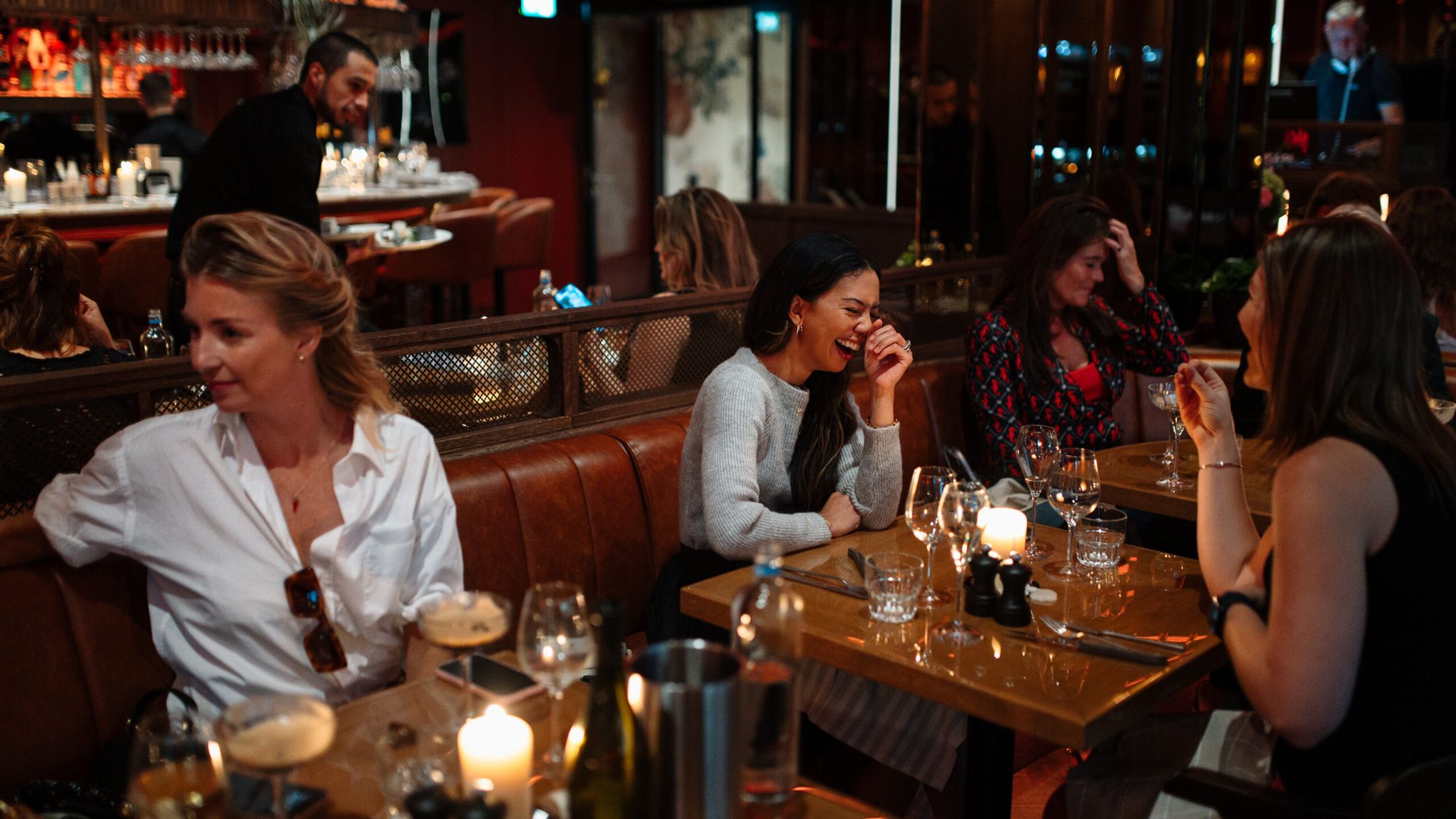 Friends laughing together at a candlelit table in a leather booth