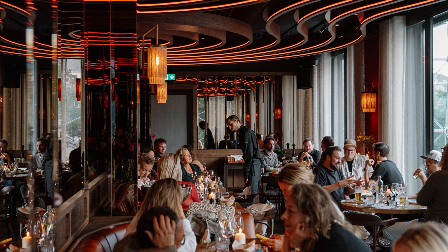 Guests dining in the Bistro under the curved, lit ceiling bands, with candles on the tables