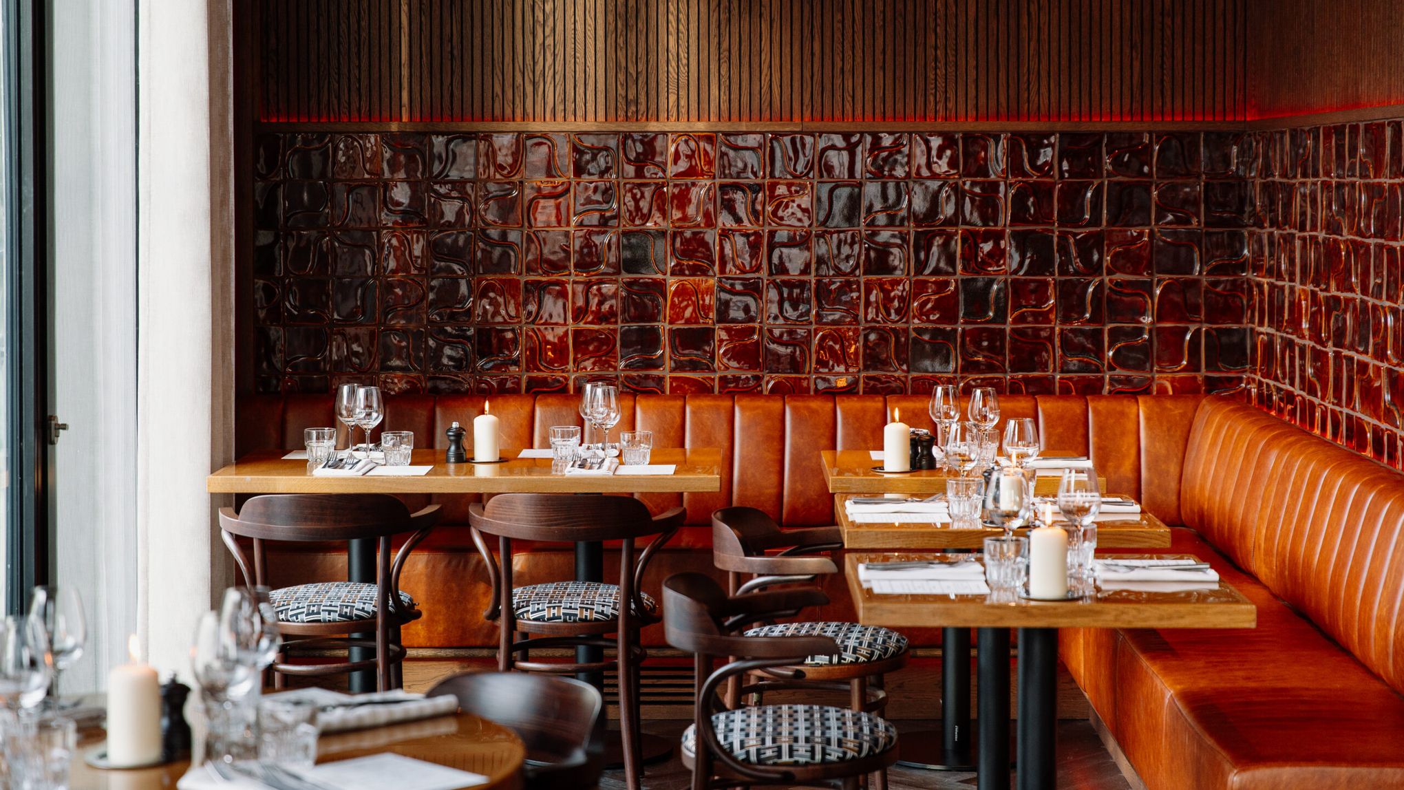 Laid tables along an orange leather banquette against a wall of dark red tiles