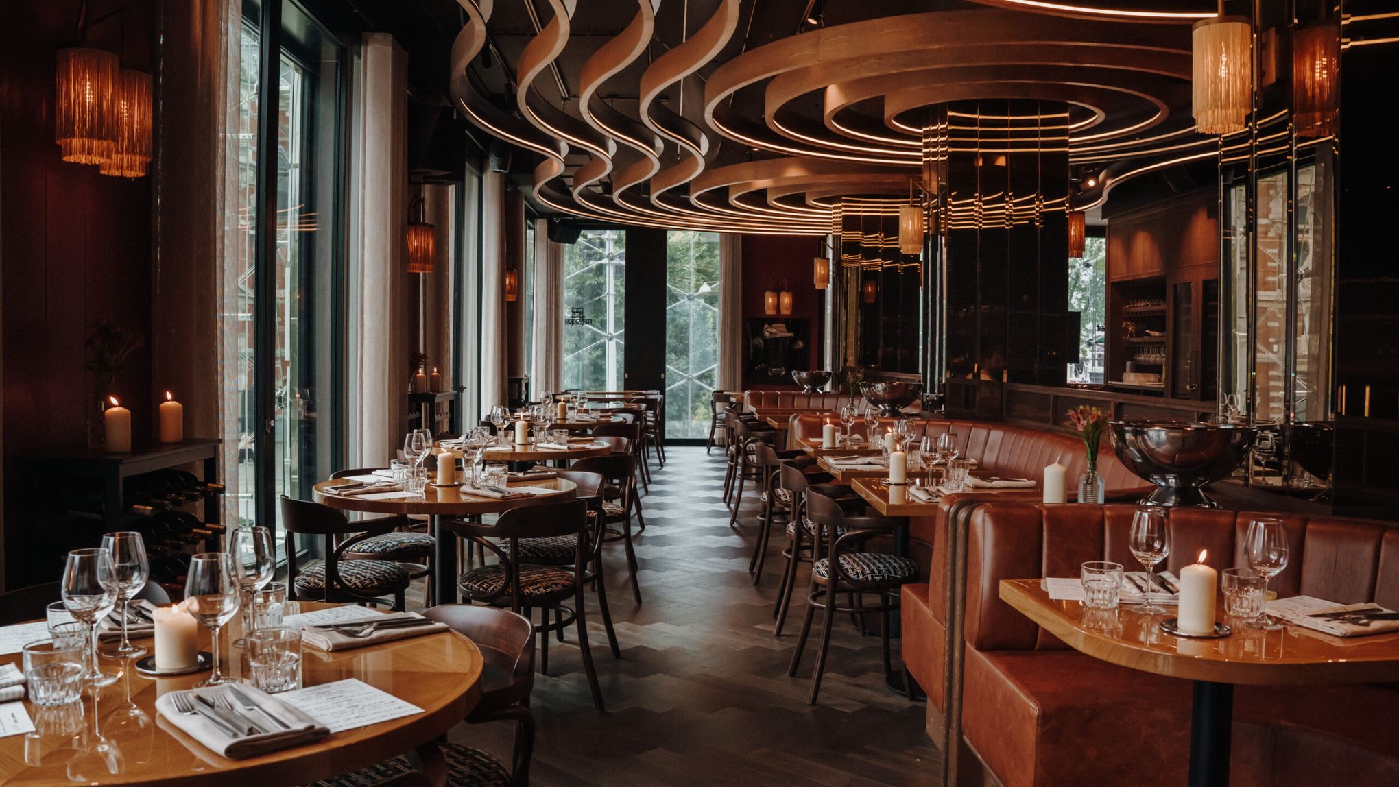 The Bistro dining room with set tables, leather banquettes, candles and curved lit ceiling bands