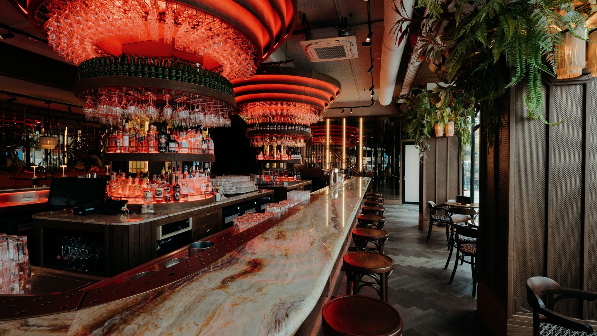 The Grand Café bar with its long marble counter, wooden bar stools and round glass racks lit in red